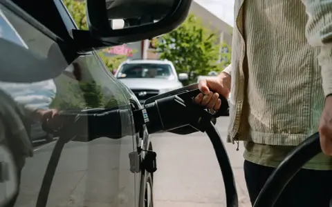 Persona che collega il cavo di ricarica a un'auto elettrica, pensando alle tariffe ricarica auto elettrica.