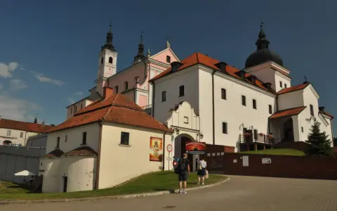 Białe budynki z czerwonymi dachami, wieże i kopuła tworzą malowniczy klasztor kamedułów.