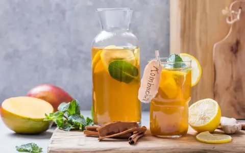 Verre et carafe de kombucha thé rafraîchissant avec des tranches de citron, de la menthe, des bâtons de cannelle et des mangues.