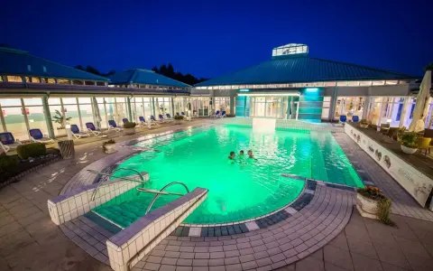 Abendliche Erfrischung im beleuchteten Pool der Therme Bad Driburg. Drei Personen genießen das warme Wasser unter dem klaren Nachthimmel.