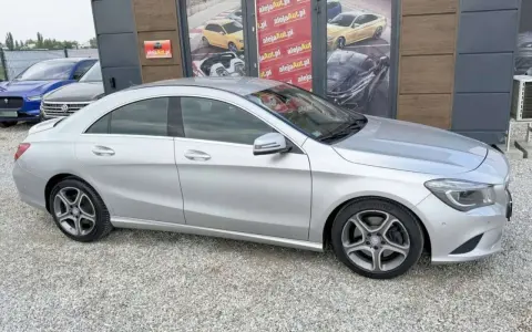Srebrny Mercedes CLA na tle salonu samochodowego z reklamami.