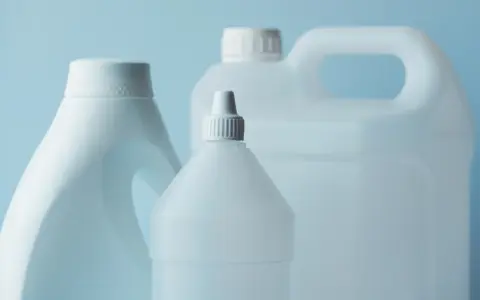 Trzy białe plastikowe butelki z uchwytami i nakrętkami na jasnoniebieskim tle.