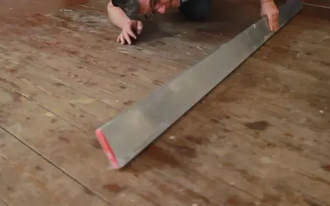 Mann verlegt Dielenboden, hält ein langes Metallwerkzeug, um die Bretter auszurichten.