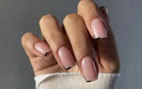 Mano con unghie quadrate naturali, smalto rosa tenue e un sottile dettaglio grafico nero sulla punta.