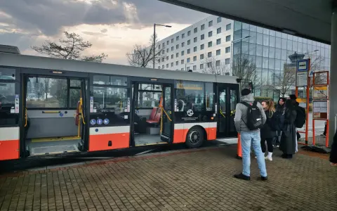 Buss vid flygplatsen, redo att ta resenärer från prag flygplats till centrum. En modern byggnad syns i bakgrunden.