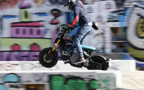 Młody mężczyzna na elektrycznym motocyklu BMW CE02 wykonuje skok na tle kolorowego graffiti.