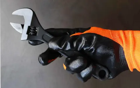 Mano enguantada sujeta llave inglesa ajustable, herramienta esencial para saber para que sirve la llave inglesa al apretar o aflojar tuercas y tornillos.
