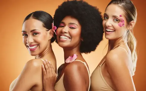 Trois femmes souriantes, un vrai "glow up traduction" avec des fleurs dans les cheveux et un maquillage éclatant.