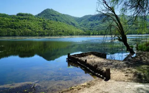 Un pontile in legno sul lago di Fimon, circondato da colline verdi e alberi.