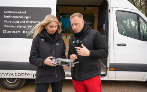 Ein Mann und eine Frau halten eine Drohnenfernbedienung. Auf dem Van stehen "Drohnenschulungen" und "Kitzrettung". Informiere dich über die drohnenführerschein kosten.