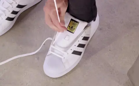Pokazuję, jak wiązać sznurówki w adidasach Superstar. Białe sznurówki przeplatane przez czarne paski.