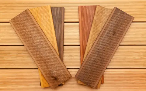 Verschiedene Holzproben mit unterschiedlichen Farben und Maserungen liegen auf einer Holzoberfläche. Sie zeigen die Vielfalt der dauerhaftigkeitsklassen holz für Terrassendielen.