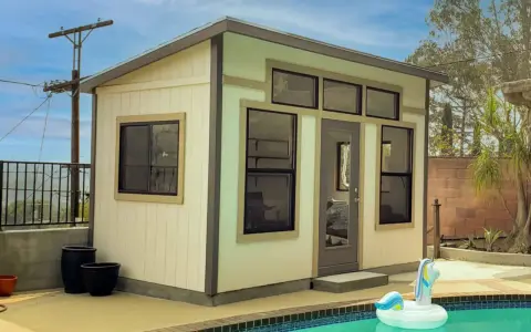 A modern shed, perfect to build a backyard oasis, sits by a pool with a unicorn float.