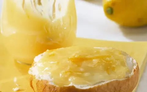 Ein Brötchen mit cremigem Lemon Curd, das ist die Antwort auf die Frage: was ist Lemon Curd. Daneben ein Glas voller dieser gelben Köstlichkeit.