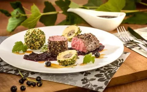 Edles Fleischgericht mit Johannisbeeren verwerten: zartes Rinderfilet, umhüllt von Kräutern und Nüssen, serviert mit einer fruchtigen Johannisbeersauce und Beilagen.