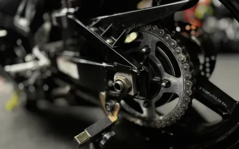 Zbliżenie na tylne koło motocykla z widocznym łańcuchem i zębatką. Pytanie: jaki smar do łańcucha motocyklowego?
