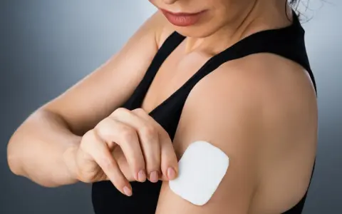 Kobieta przykleja plaster antykoncepcyjny na ramię. Poznaj, jak działają plastry antykoncepcyjne, uwalniając hormony przez skórę.