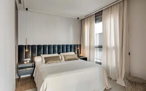 Acogedora habitación pequeña con cama grande, cabecero tapizado, mesitas de noche modernas y cortinas elegantes.