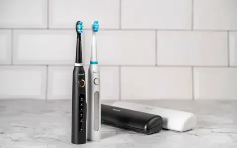 Dwa eleganckie modele szczoteczek sonicznych, czarny i srebrny, z różnymi końcówkami do wyboru. Obok etui podróżne.