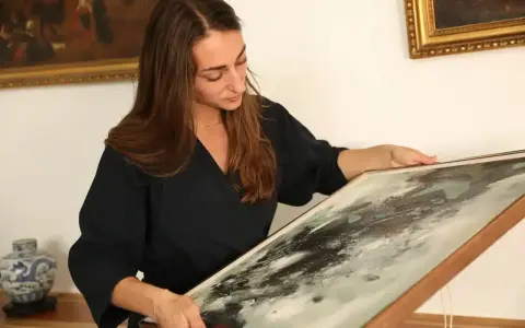 Une femme examine un tableau abstrait, cherchant des indices pour comment estimer un tableau avec signature.