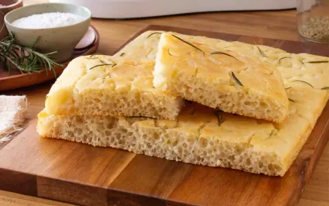 Focaccia senza glutine soffice e dorata, guarnita con rosmarino fresco, pronta per essere gustata.