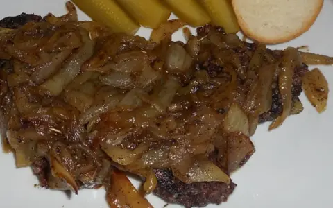 Kaszanka z cebulą, podana z ogórkami kiszonymi i kromką chleba. Danie wygląda apetycznie i sycąco.