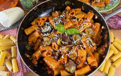 Rigatoni ricchi di melanzane fritte e pomodoro, conditi con ricotta salata grattugiata e basilico fresco. Un piatto di pasta alla norma invitante.