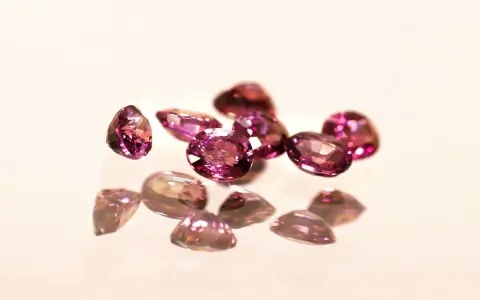 Un gruppo di pietre di granato rosa sfaccettate, che riflettono la luce su una superficie lucida.