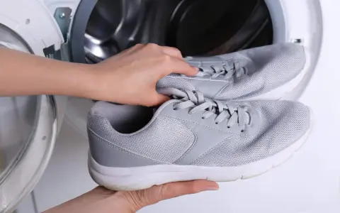 Ręce wkładają szare adidasy do pralki. Dowiedz się, jak prać adidasy w pralce, aby odświeżyć swoje ulubione buty.