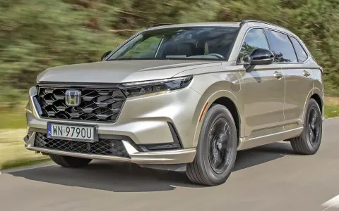 Nowy Honda CR-V w kolorze złotym jedzie po drodze, otoczony zielenią.