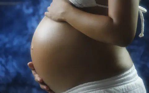 Pancia di donna incinta, con mani che la accarezzano. Si intravede un bikini bianco e uno sfondo blu. L'addome è tonico, forse con un leggero intestino iperecogeno visibile.