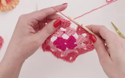 Händer virkar ett rosa virkat zigzag filt mönster med en virknål.