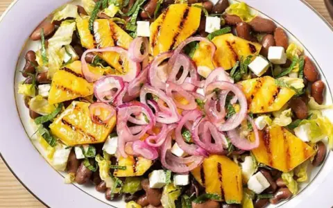 Ensalada de frijoles, piña a la parrilla, queso y cebolla morada en un plato blanco.