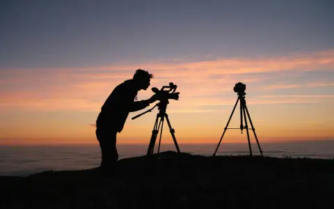 Sylwetka fotografa z kamerą na statywie o zachodzie słońca. Zastanawiasz się, ile zarabia fotograf miesięcznie?
