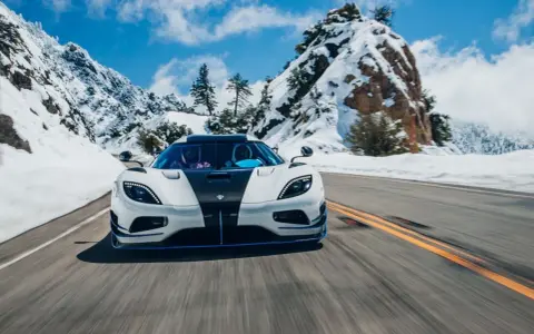Biały Koenigsegg Agera RS z czarnym pasem na masce pędzi po ośnieżonej górskiej drodze.