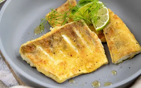 Zanderfilet ohne Haut braten: goldbraune Fischfilets auf grauem Teller, garniert mit Dill und Limettenspalten.