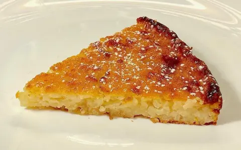 Una fetta di torta di riso, profumata e dorata, come la torta di riso ricetta della nonna, spolverata di zucchero a velo.