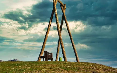 Un columpio ríachuelo solitario en la cima de una colina, con un banco y una mochila verde, bajo un cielo dramático.