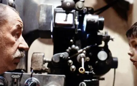 Un uomo e un bambino osservano affascinati una vecchia cinepresa, un'immagine che evoca le magiche tecniche cinematografiche.