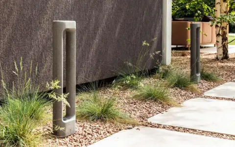 Deux bornes d'éclairage modernes en béton, bordant un chemin. L'ensemble respecte la norme éclairage lux pour un jardin contemporain.