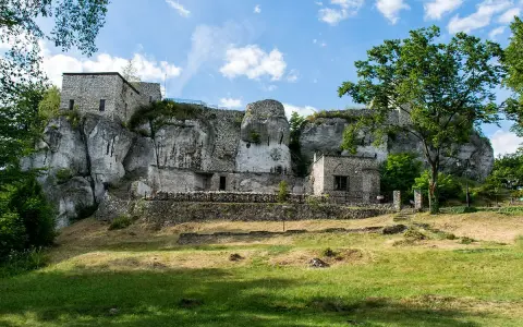 Kamienny zamek morsko wznosi się na skale, otoczony zielenią. Ruiny i mury tworzą malowniczy krajobraz.