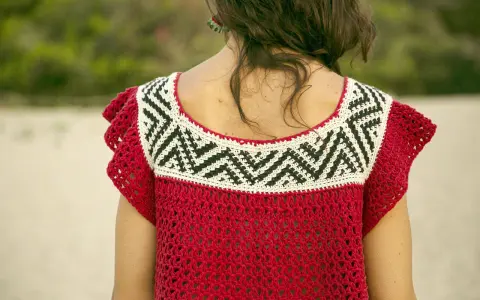 Detalle de un top de ganchillo rojo con un patrón geométrico blanco y negro en el cuello.