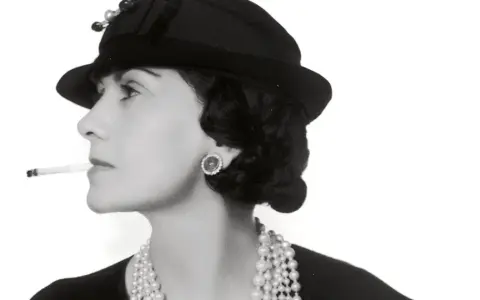 Coco Chanel, con sigaretta e perle, icona di stile, ci ricorda dove è nata Coco Chanel, un'ispirazione senza tempo.