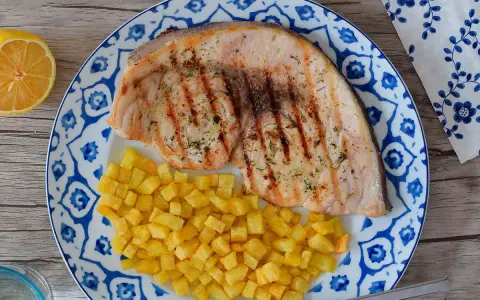 Delicioso emperador a la plancha con patatas fritas crujientes, servido en un plato con diseño azul y blanco. Un toque de limón completa esta apetitosa presentación.