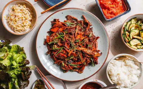 Ein köstliches koreanisches BBQ-Rezept mit gebratenem Fleisch, Beilagen wie Kimchi, Gurkensalat, Sprossen und Reis.