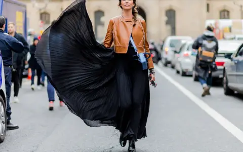 Donna con gonna nera plissettata e giacca in pelle marrone, un look audace che esprime la sua lybido abbigliamento.