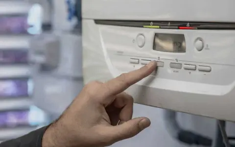 Mano presionando un botón en la caldera de gas, indicando posibles problemas. La pantalla muestra "02".