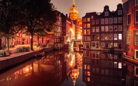 Nocny Amsterdam, kanał odbija oświetlone kamienice i kopułę kościoła. Czerwona ulica Amsterdam w blasku latarni.