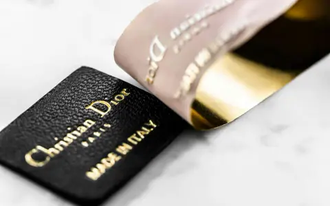 Etichetta in pelle nera con logo Christian Dior Paris e "Made in Italy" dorato, accanto a un nastro Dior francese con finitura oro lucido.