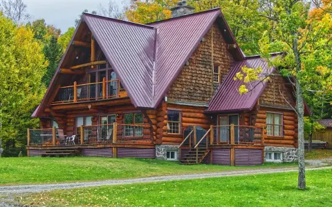 Chalet en bois rond avec toiture métallique, entouré d'arbres aux couleurs d'automne. Un exemple de développement durable bâtiment, alliant esthétique et respect de l'environnement.